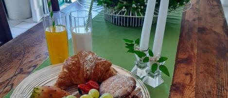 A breakfast setting with a plate of food, a glass of orange juice, a glass of milk, and a croissant on a wooden table.