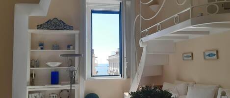 Una sala de estar acogedora con una escalera, una ventana con vistas y un sofá blanco, además de objetos decorativos.