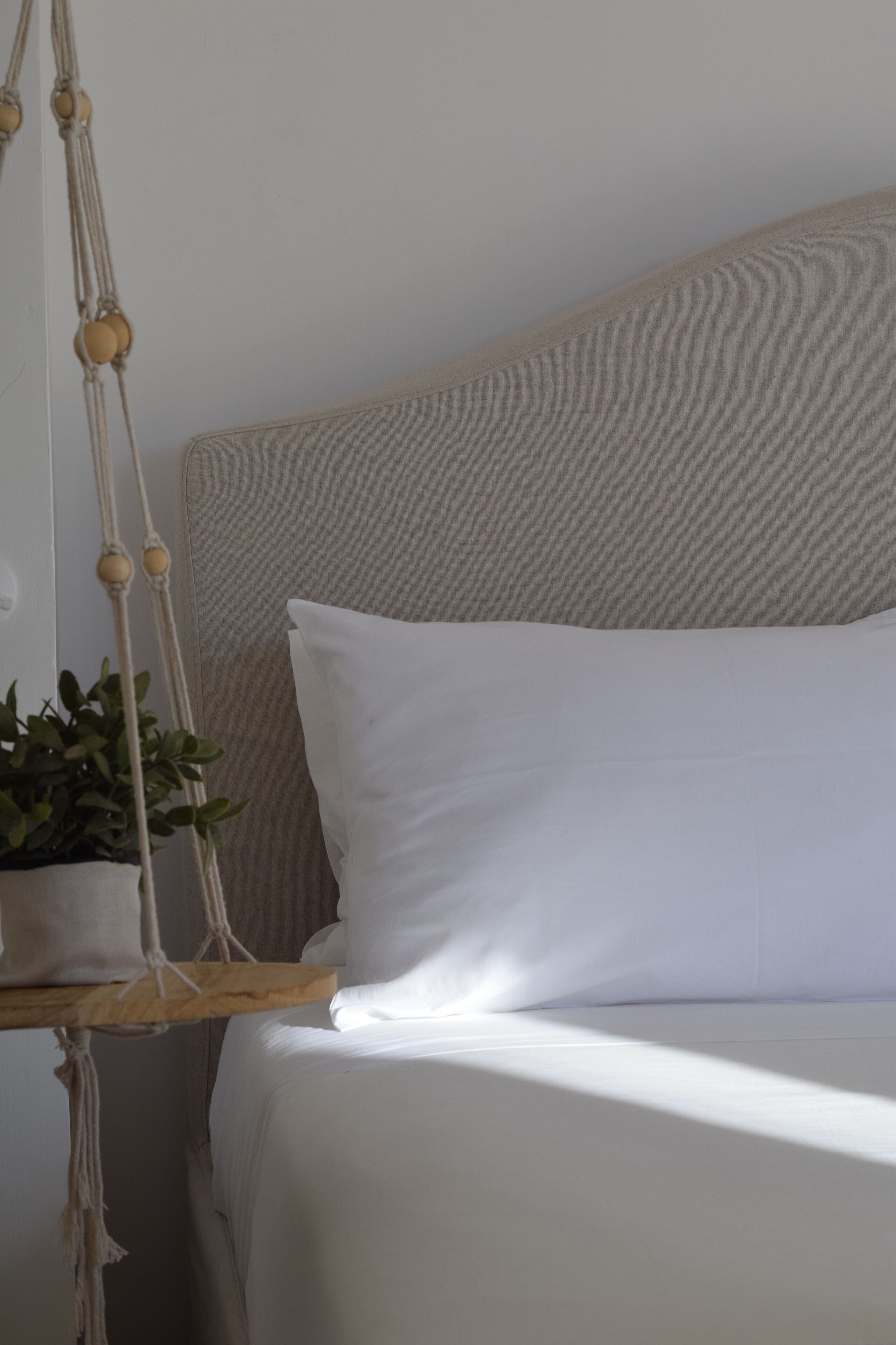 A bed with white bedding, a macrame wall hanging, and a potted plant.