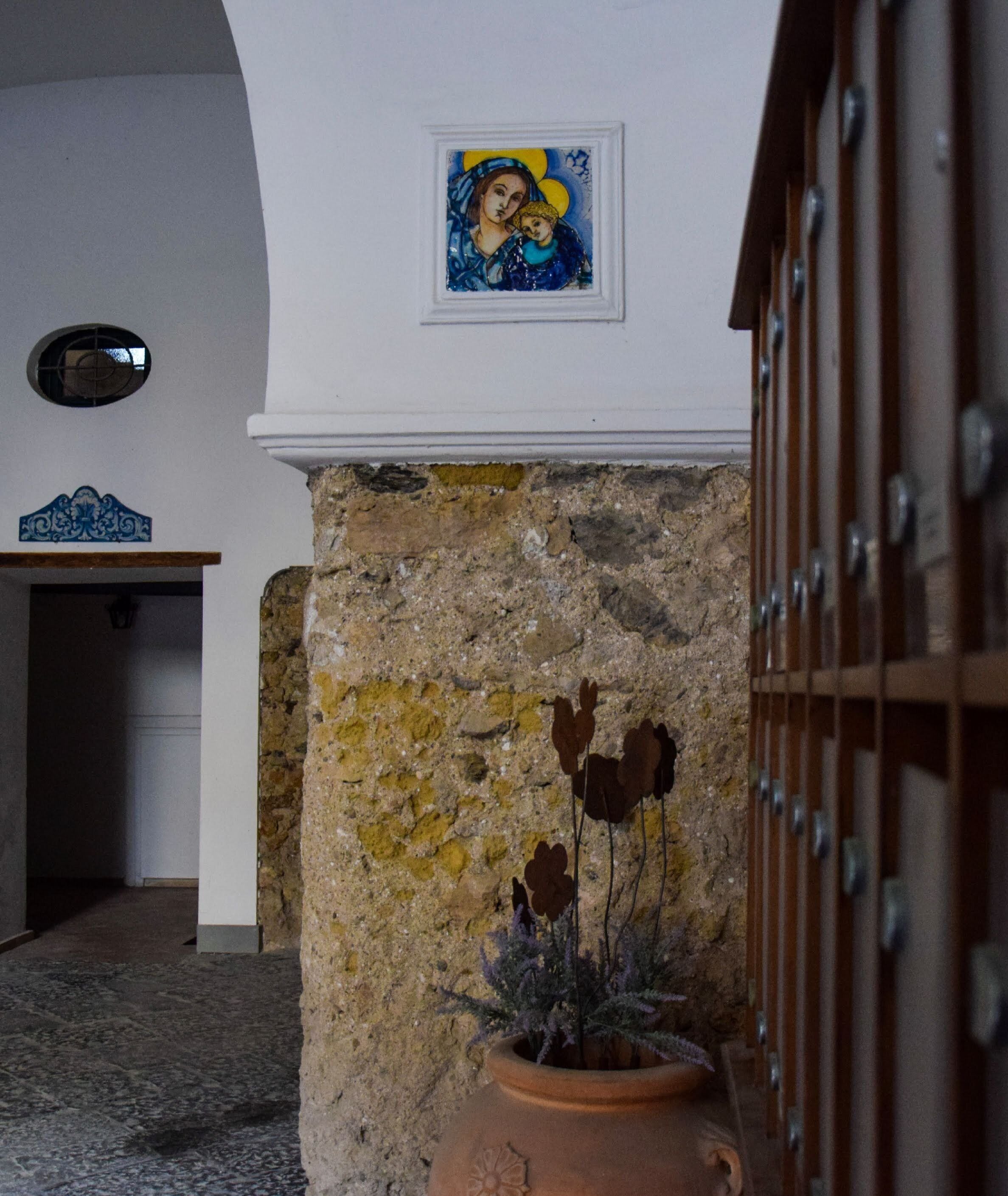 A stone wall with a potted plant and a framed artwork above it.