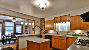 A kitchen with wooden cabinets, a central island, and a dining area with chairs. - Chequamegon Haus - Comfortable and Charming walk to downtown Cable, WI (Cable)