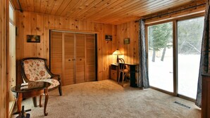 A wooden-paneled room with a large sliding glass door to the outside, a wooden chair, a small table, and a lamp. - Chequamegon Haus - Comfortable and Charming walk to downtown Cable, WI (Cable)