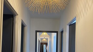 A hallway with a wooden floor, white walls, and a ceiling light fixture.