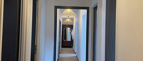 A hallway with a wooden floor, white walls, and a ceiling light fixture.