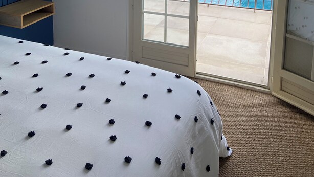 A bedroom with a bed, a window, and a view of a swimming pool and greenery.