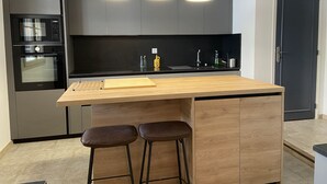 A modern kitchen with grey cabinets, a black countertop, a wooden island with stools, and a black oven.
