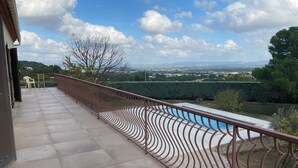 A balcony with a view of a swimming pool and distant landscape.