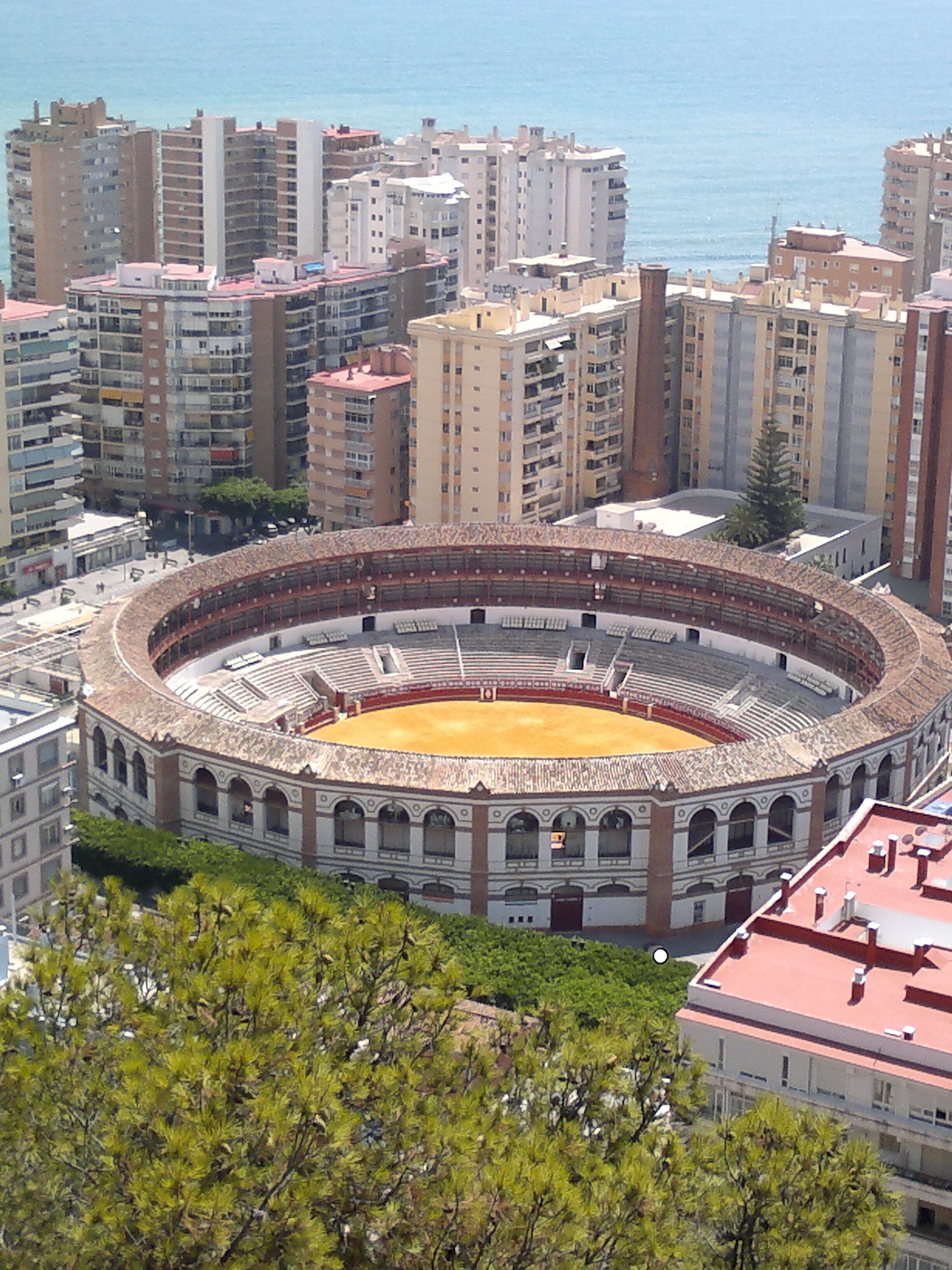 Une arène de corrida entourée d’immeubles de grande hauteur, offrant une vue dégagée sur l’intérieur et l’extérieur de l’arène.