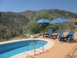 Relax by the pool surrounded by lounge chairs and umbrellas, with a beautiful view of the hilly landscape.