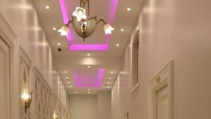 A hallway with white walls, patterned wallpaper, and a chandelier. There are potted plants along the sides and a door at the end. - New Midtown Hotel (Cairo)