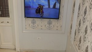 A dining area with two chairs, a table with plates of food, and a television mounted on the wall displaying a scene with a boat. - New Midtown Hotel (Cairo)