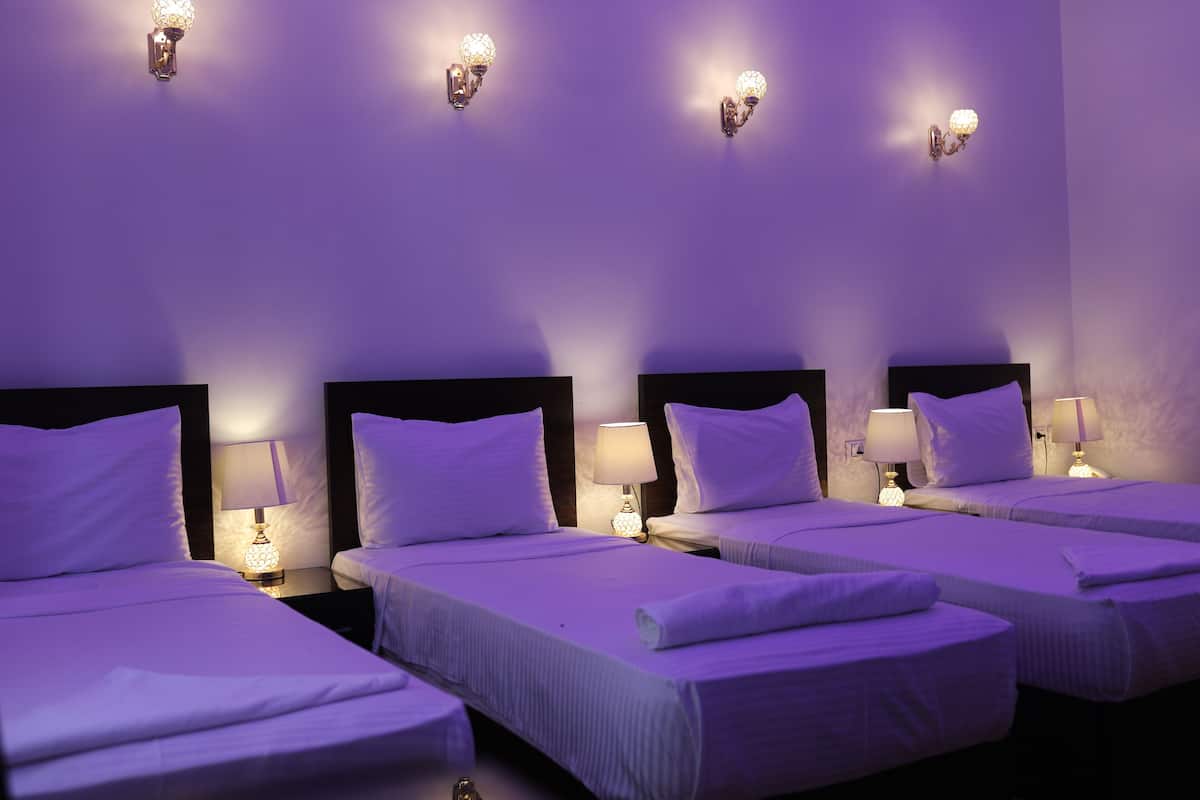 A hotel room with four single beds, each with a nightstand and a lamp.