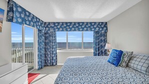 A bedroom with a large bed, a view of the sea, and a balcony. - Oceanfront Condo in Cherry Grove. Enjoy fun in the sun! Reduced Rates! (North Myrtle Beach)
