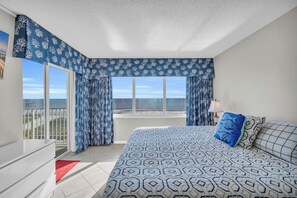 A bedroom with a large bed, a view of the sea, and a balcony. - Oceanfront Condo in Cherry Grove. Enjoy fun in the sun! Reduced Rates! (North Myrtle Beach)