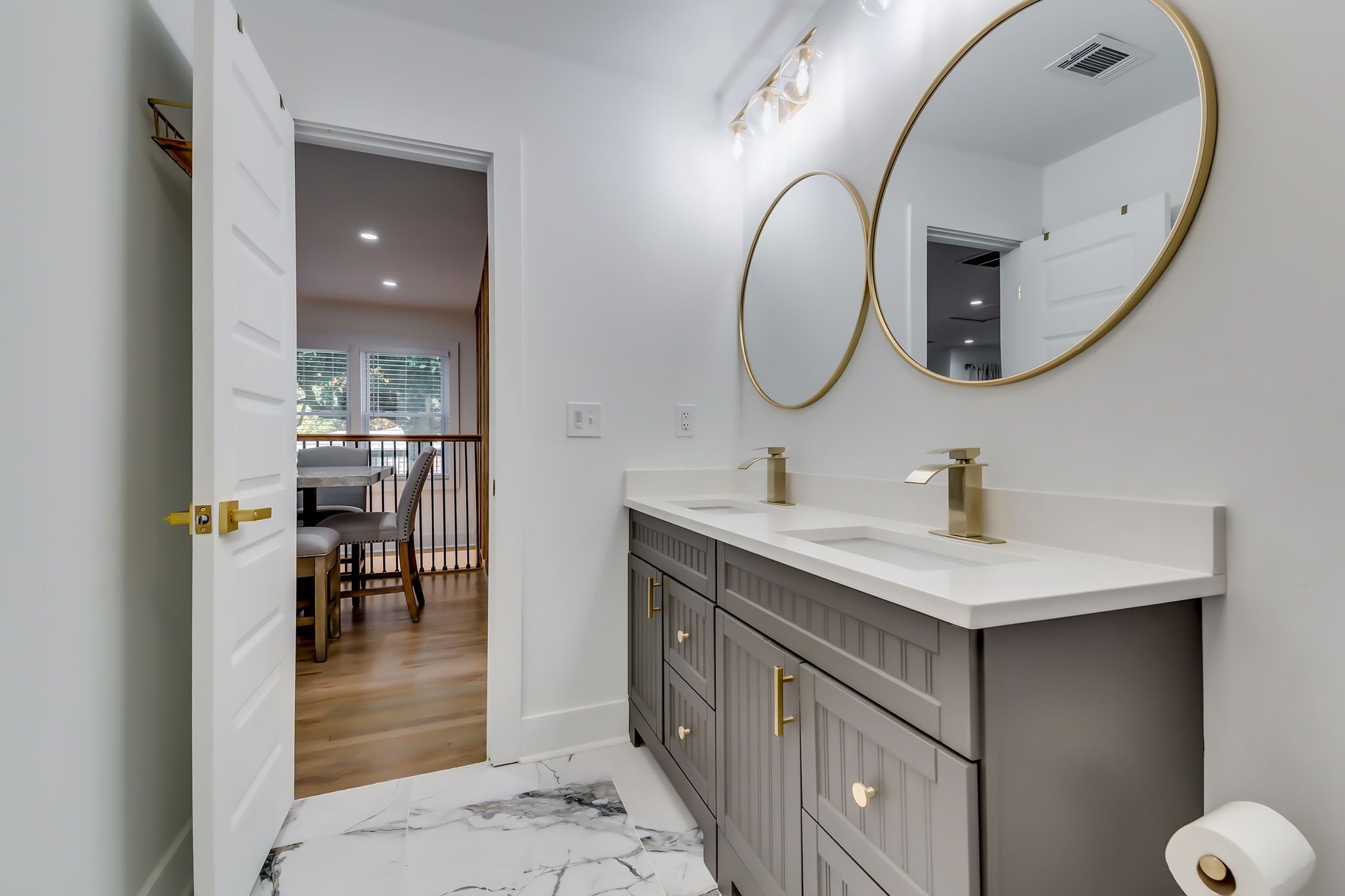 Un baño moderno con dos espejos redondos, un lavabo blanco y suelo de baldosas de mármol.