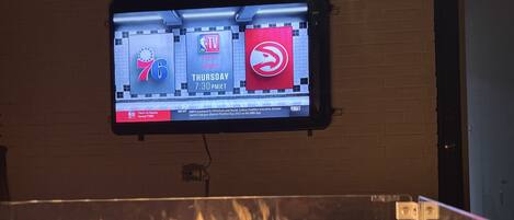 Televisiossa näkyy NBA-ottelu, jossa pelaavat Hawks ja 76ers, ja kuvan etualalla näkyy tuli.