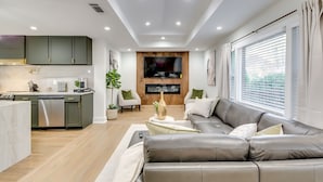 Uma sala de estar moderna com sofá, televisão e área de cozinha com armários e lava-louças.