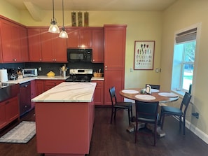 A kitchen with red cabinets, a central island, a dining table with chairs, a microwave, and a stove. - Cozy Casita with spectacular view of the sunset (Sherman)