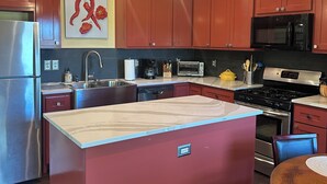 A kitchen with a central island, stainless steel appliances, and red cabinets.