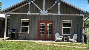 A building with a red door, two windows, and a covered porch with Adirondack chairs.