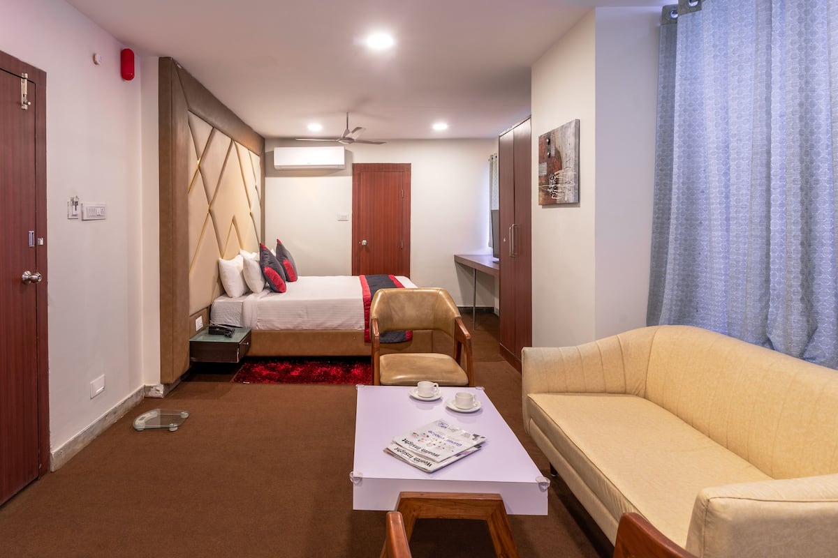 A compact hotel room with a bed, a sofa, a small table, and a desk.