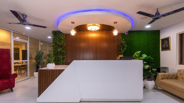 Un espace d’accueil doté d’un comptoir de réception blanc, de ventilateurs de plafond et d’éléments décoratifs verts sur les murs.