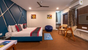 Une chambre d’hôtel moderne avec un lit, un fauteuil en forme de poire bleu, une chaise en bois et un téléviseur à écran plat.
