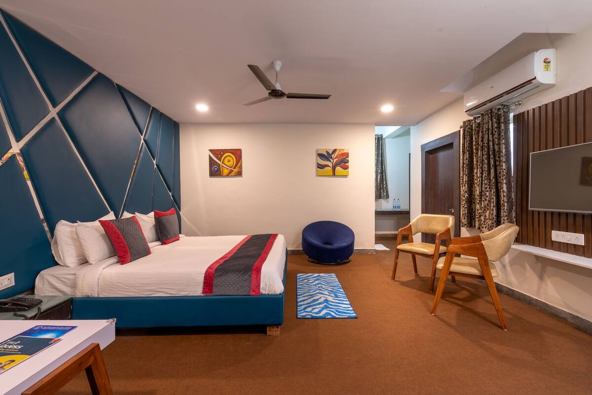 A modern hotel room with a bed, a blue bean bag chair, a wooden chair, and a flat-screen TV.