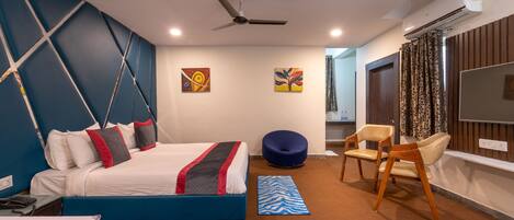 A modern hotel room with a bed, a blue bean bag chair, a wooden chair, and a flat-screen TV.