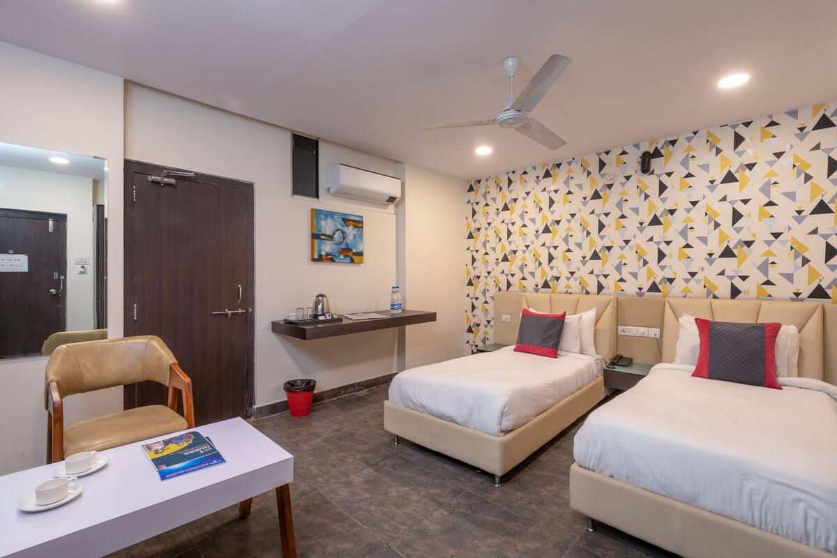 A hotel room with two beds, a desk with a chair, a ceiling fan, and a patterned wall.
