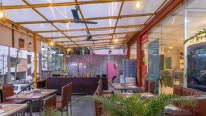 Un restaurant doté d’un mur en verre, d’un plafond jaune et d’un espace où sont disposées des tables et des chaises.