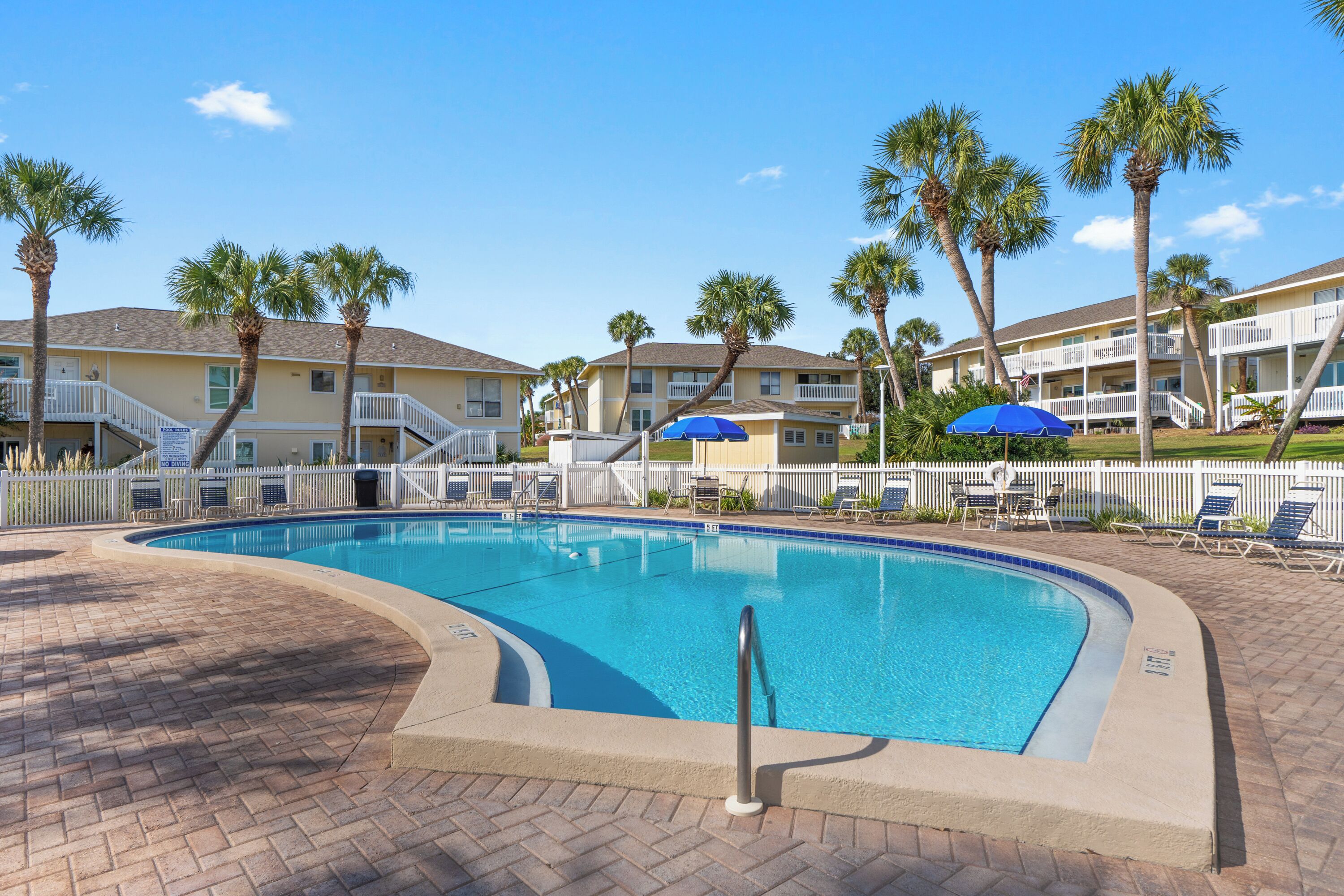 A swimming pool with a brick deck, surrounded by palm trees and lounge chairs.