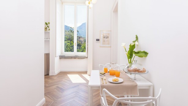 A bright dining area with a table set for breakfast, a window with a mountain view, and a vase with flowers. - Lux Aurea (Meta)