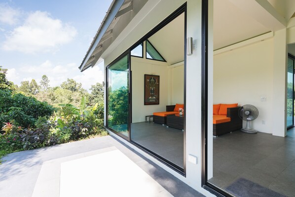 A modern house with large glass doors leading to a living area with a sofa and a fan.