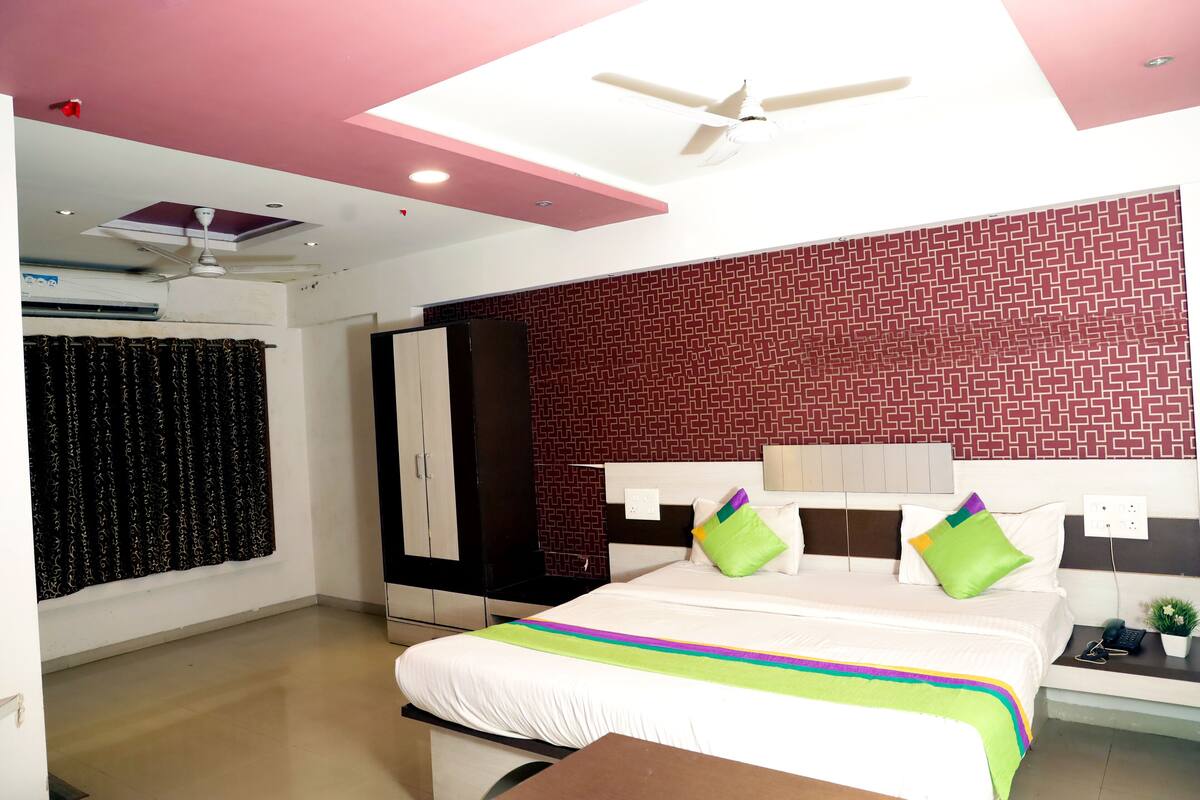 A hotel room with a bed, a wardrobe, a ceiling fan, and a patterned wall.