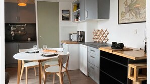 A modern kitchen with a dining area, featuring a wooden table, chairs, and a coffee machine. - Cosy studio with panoramic terrace & parking (Tours)