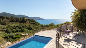 Un espace aménagé au bord de la piscine, offrant une vue sur la mer et les collines.