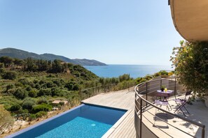 Uma área à beira da piscina com vista para o mar e colinas.