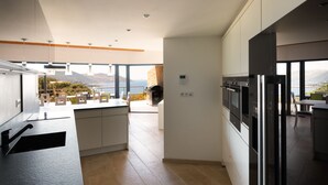 Une cuisine moderne avec vue sur la mer, un coin repas avec une table et des chaises, et un grand réfrigérateur.