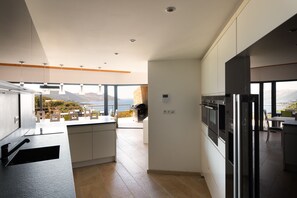 Cozinha moderna com vista para o mar, sala de jantar com mesa e cadeiras, e uma geladeira grande.