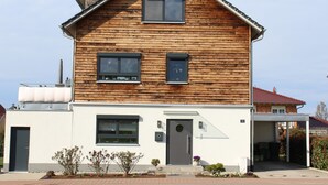 Een houten woonhuis met twee verdiepingen, een puntig dak, een voordeur en twee ramen op de tweede etage.