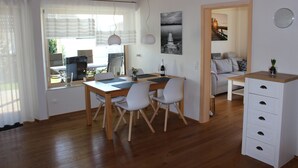 Een moderne leefruimte met een houten eettafel, witte stoelen, een witte kast en uitzicht op het omliggende landschap door grote ramen.