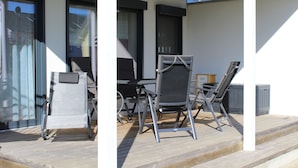 Een overdekt terras met een tafel en stoelen, een kleine tafel met een stoel, en een raam met zonwering.