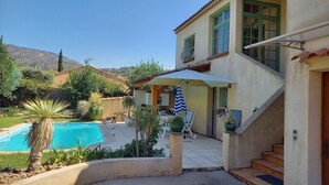 A two-story house with a pool, outdoor seating, and a staircase leading to the upper floor.