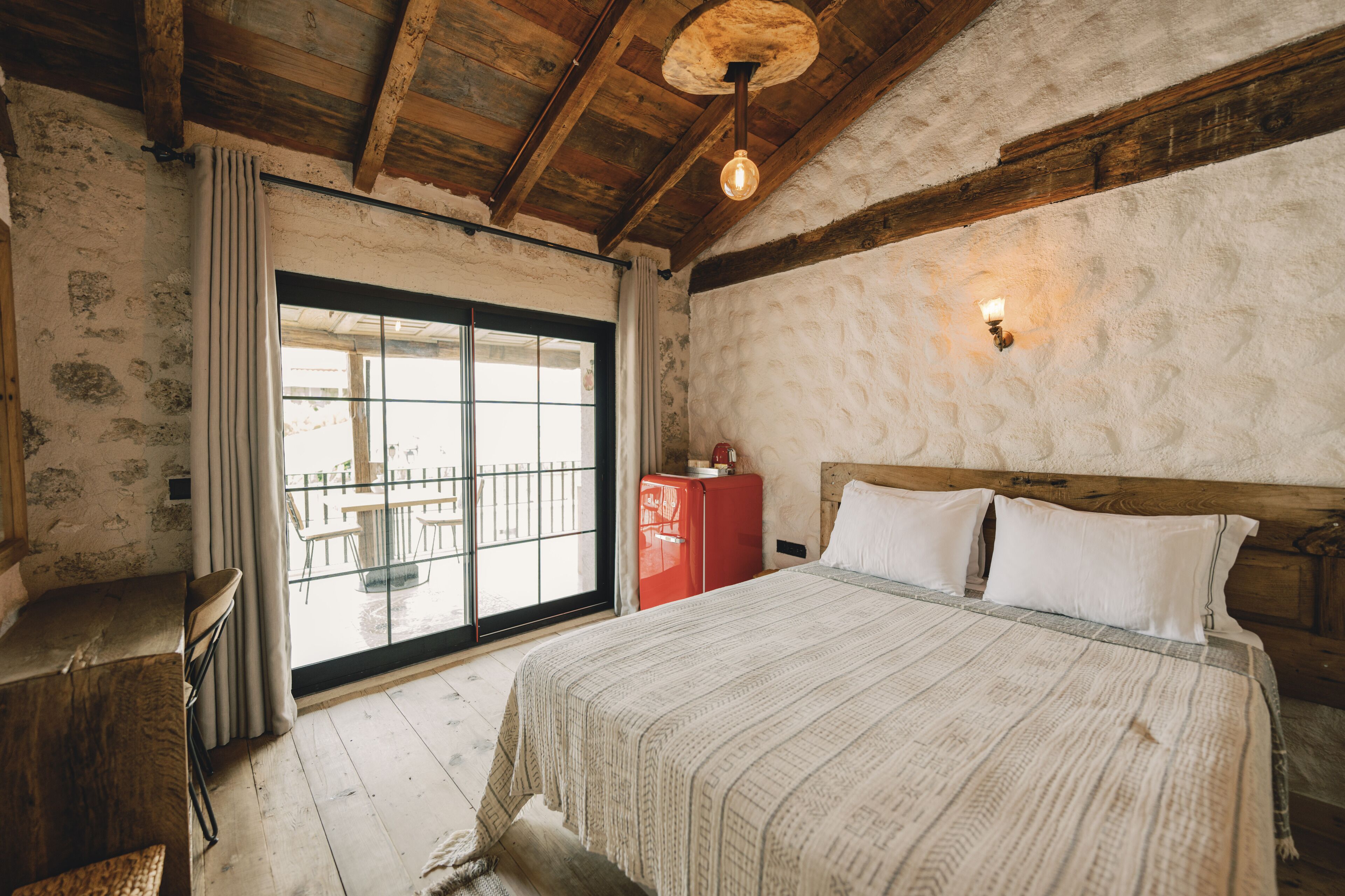 Une chambre avec un plafond en bois, un lit avec une literie blanche, une armoire rouge et une vue sur un espace extérieur, visible à travers une porte vitrée.