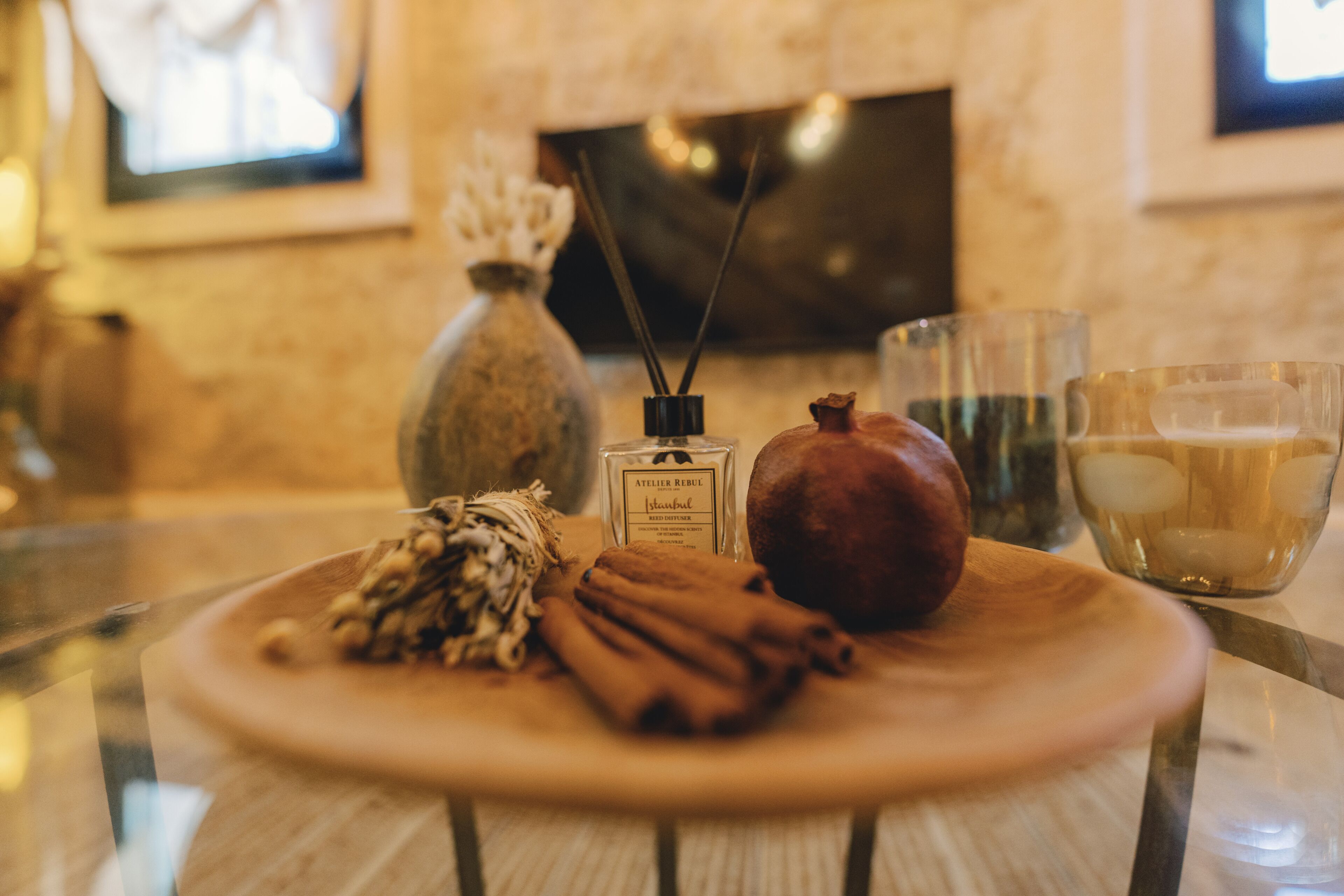 A wooden table with a plate containing cinnamon sticks, a pomegranate, and a bottle of perfume.