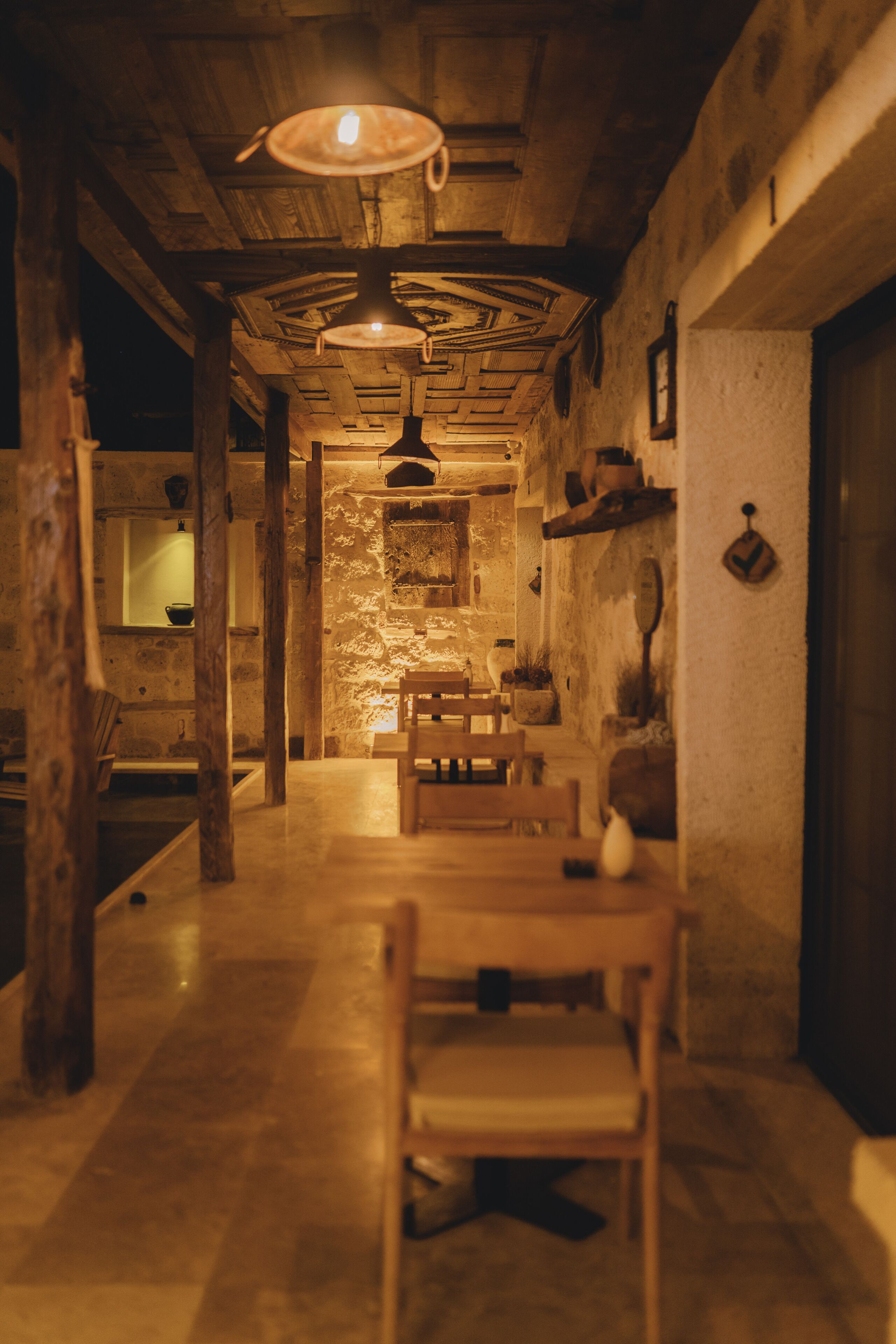 A rustic interior with a wooden dining table, benches, and a stone wall.