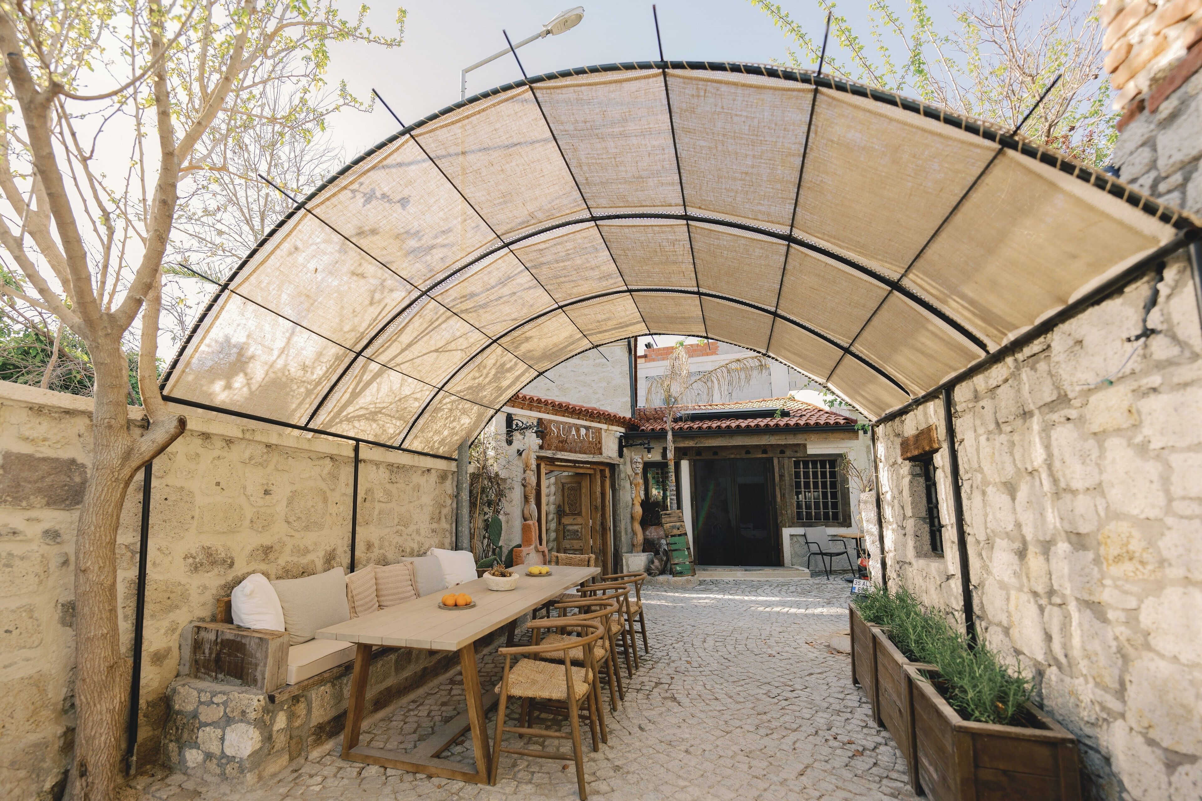 A covered outdoor dining area with a stone wall, wooden furniture, and a table with fruits.