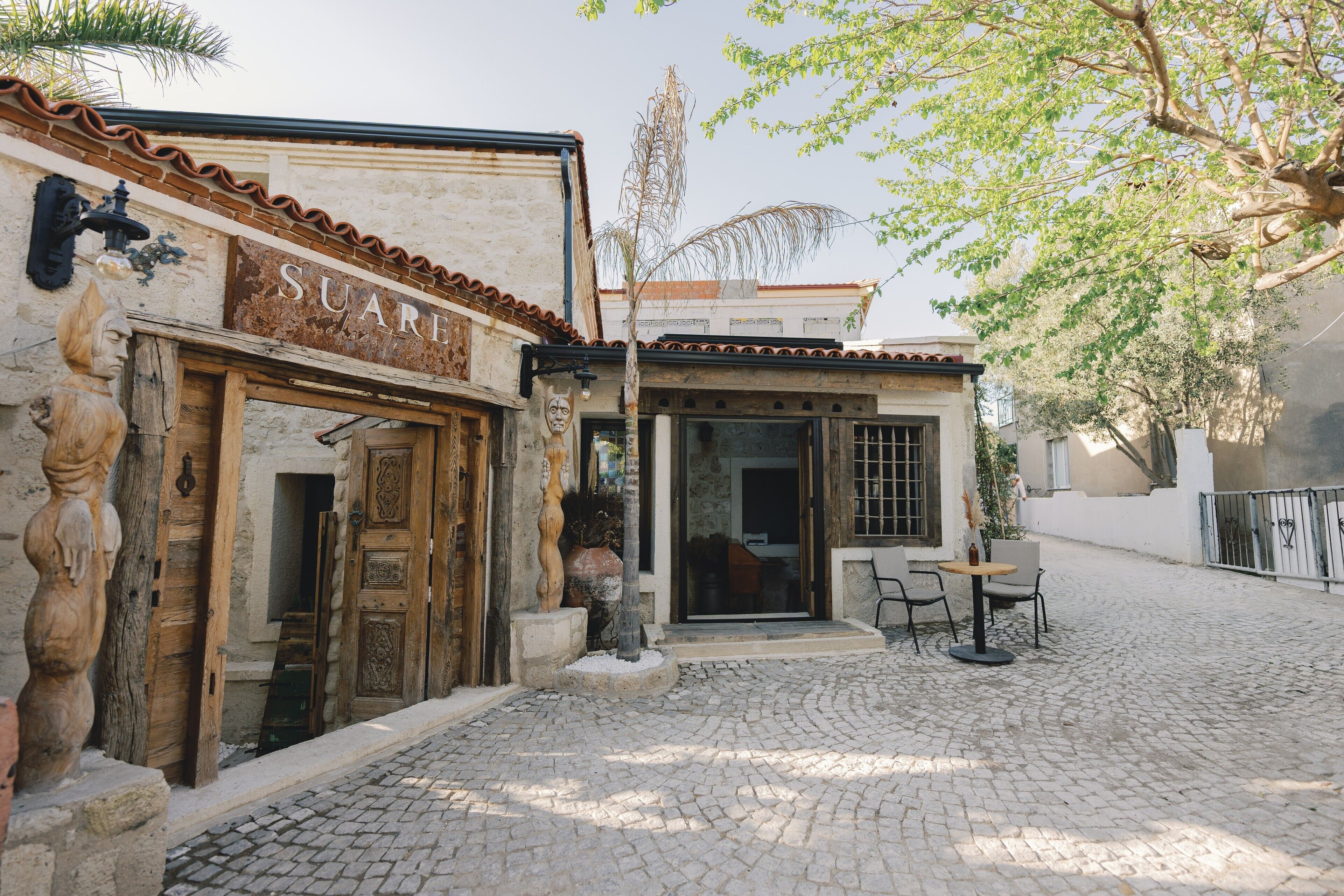 A cobblestone courtyard with a rustic building featuring a wooden door and a sign that reads "SUARE".