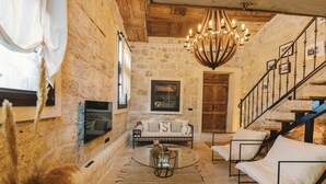 A rustic stone interior with a wooden staircase, a chandelier, a sofa, and a coffee table. - Suare Alaçatı (Cesme)